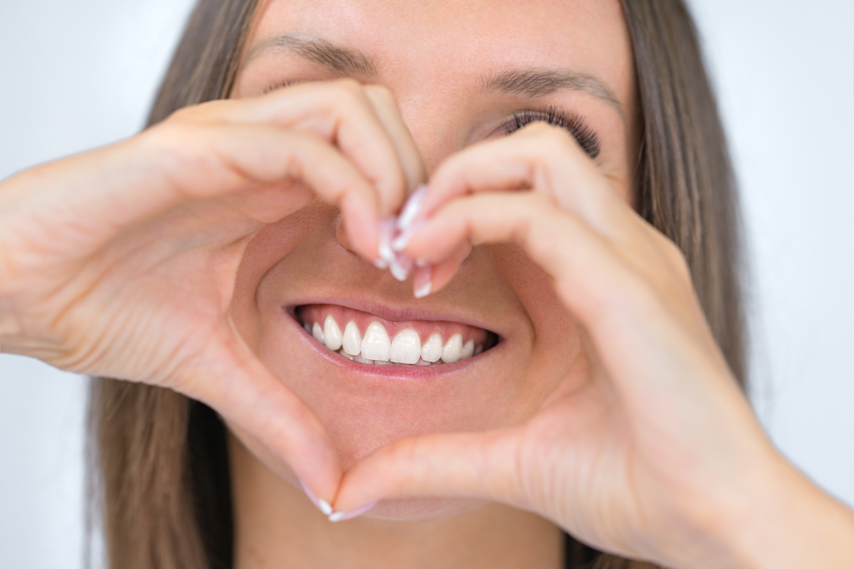 Woman With Healthy Teeth and Hands Forming Heart Shape